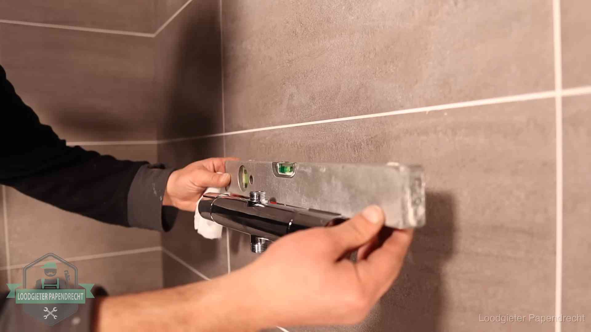 Loodgieter lijnt een douchekraan uit met een waterpas in een woning in Papendrecht