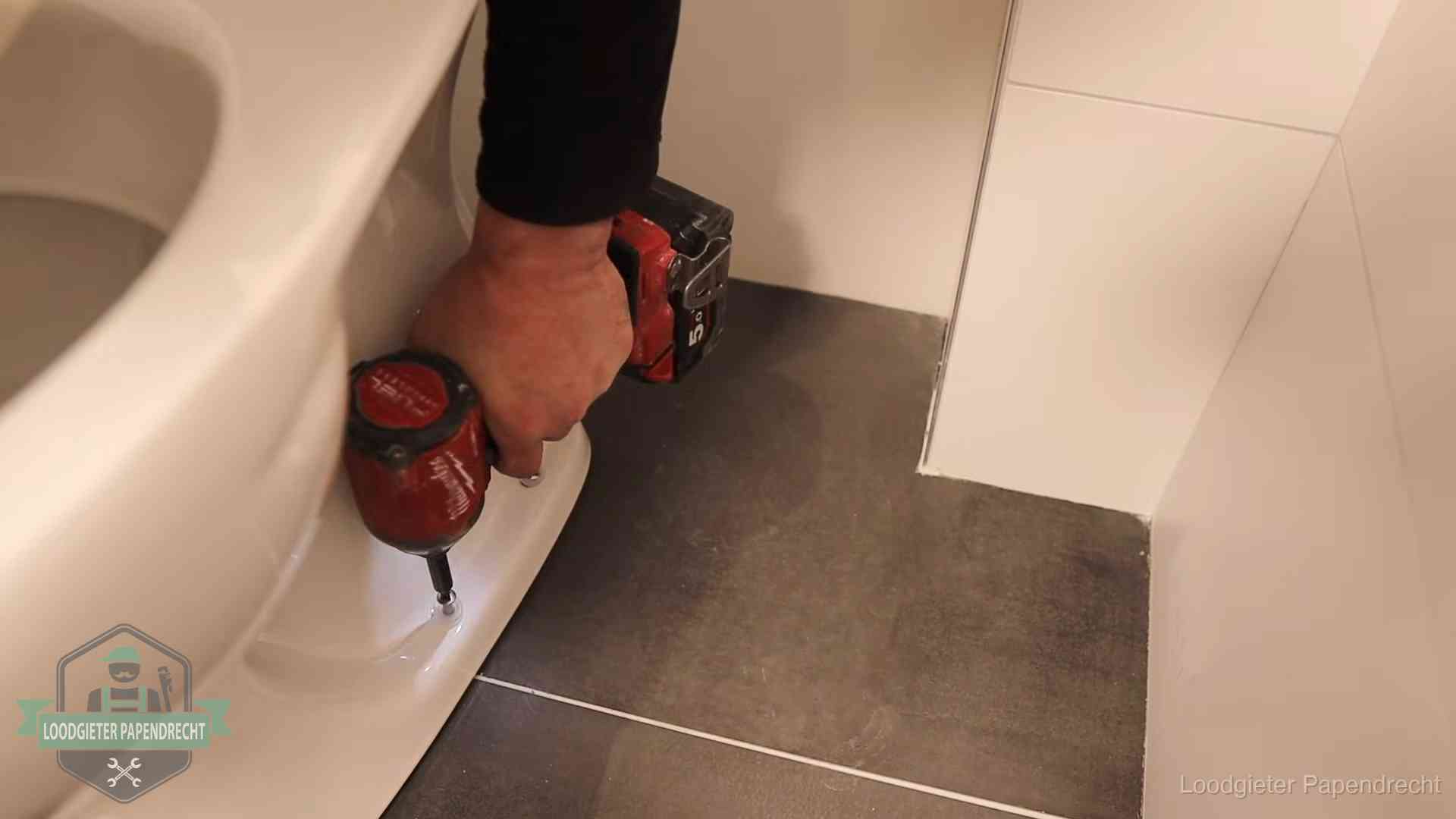 Kosten wc ontstoppen in Papendrecht Loodgieter zet de voet van een wc-pot vast op de tegelvloer in Papendrecht